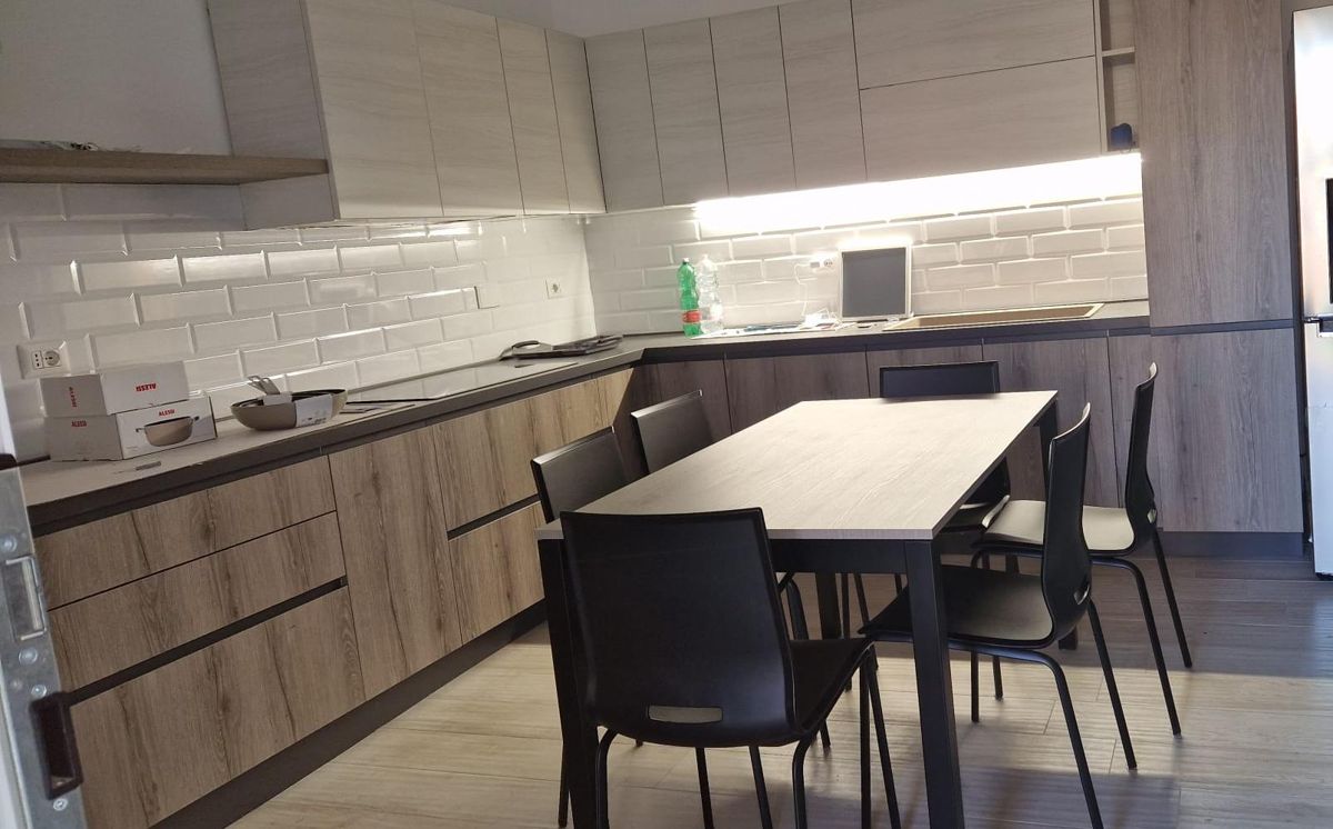 Dopo: la stessa cucina arredata, con mobili in legno, tavolo e sedie