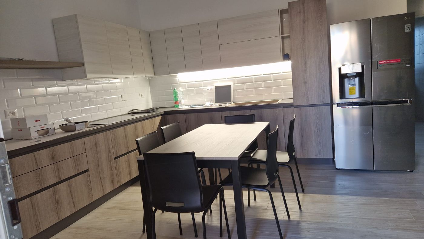 Cucina arredata con mobili in legno, rivestimento bianco diamantato e tavolo con sedie nere