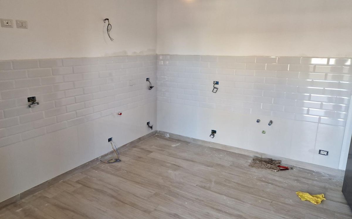 Prima: cucina a fine cantiere con rivestimento bianco, pavimento effetto legno e predisposizioni degli impianti